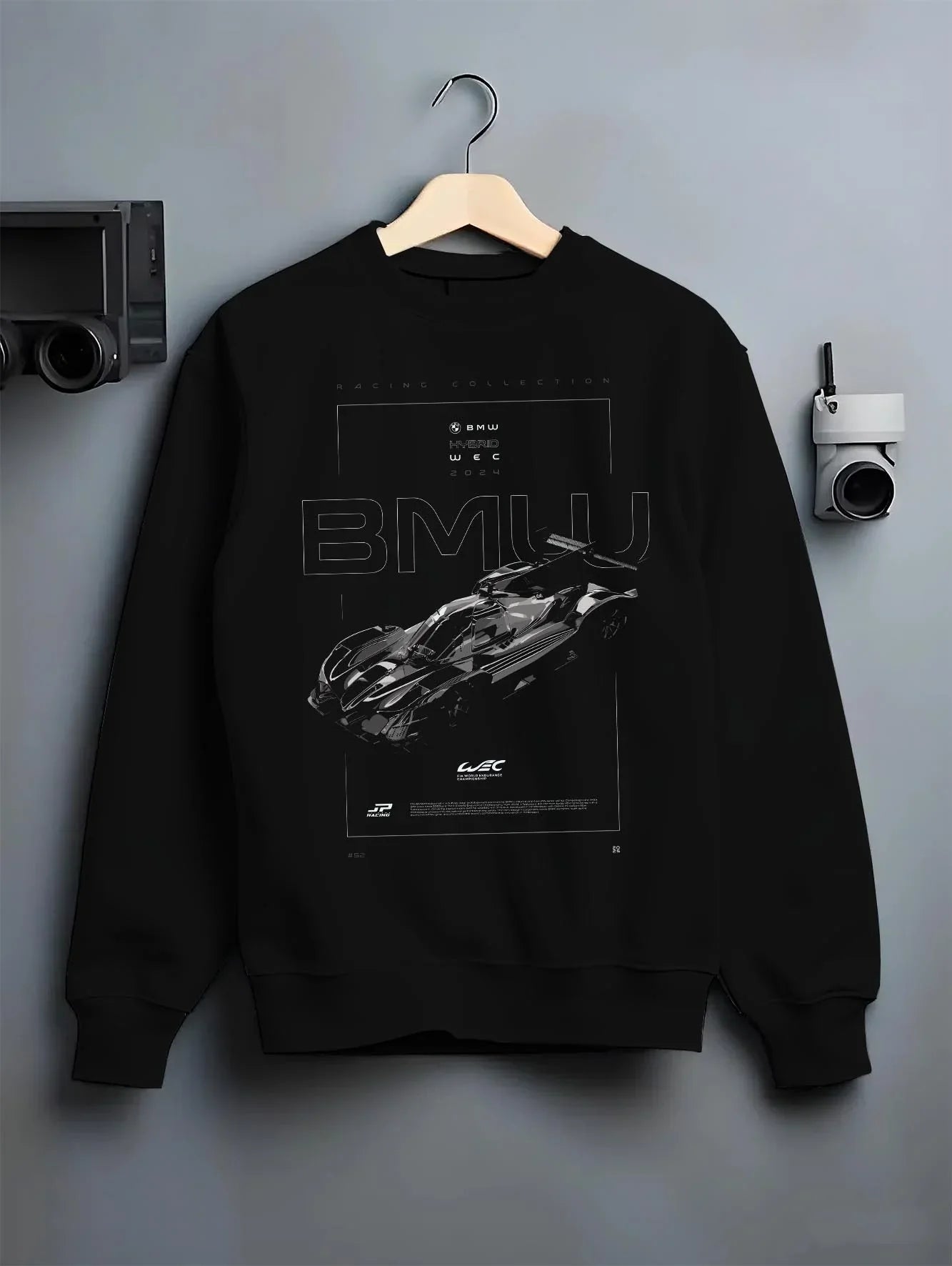 Black crewneck sweatshirt on a hanger against a grey wall, featuring BMW 202 rs racing le mans motorsport german street graphic.