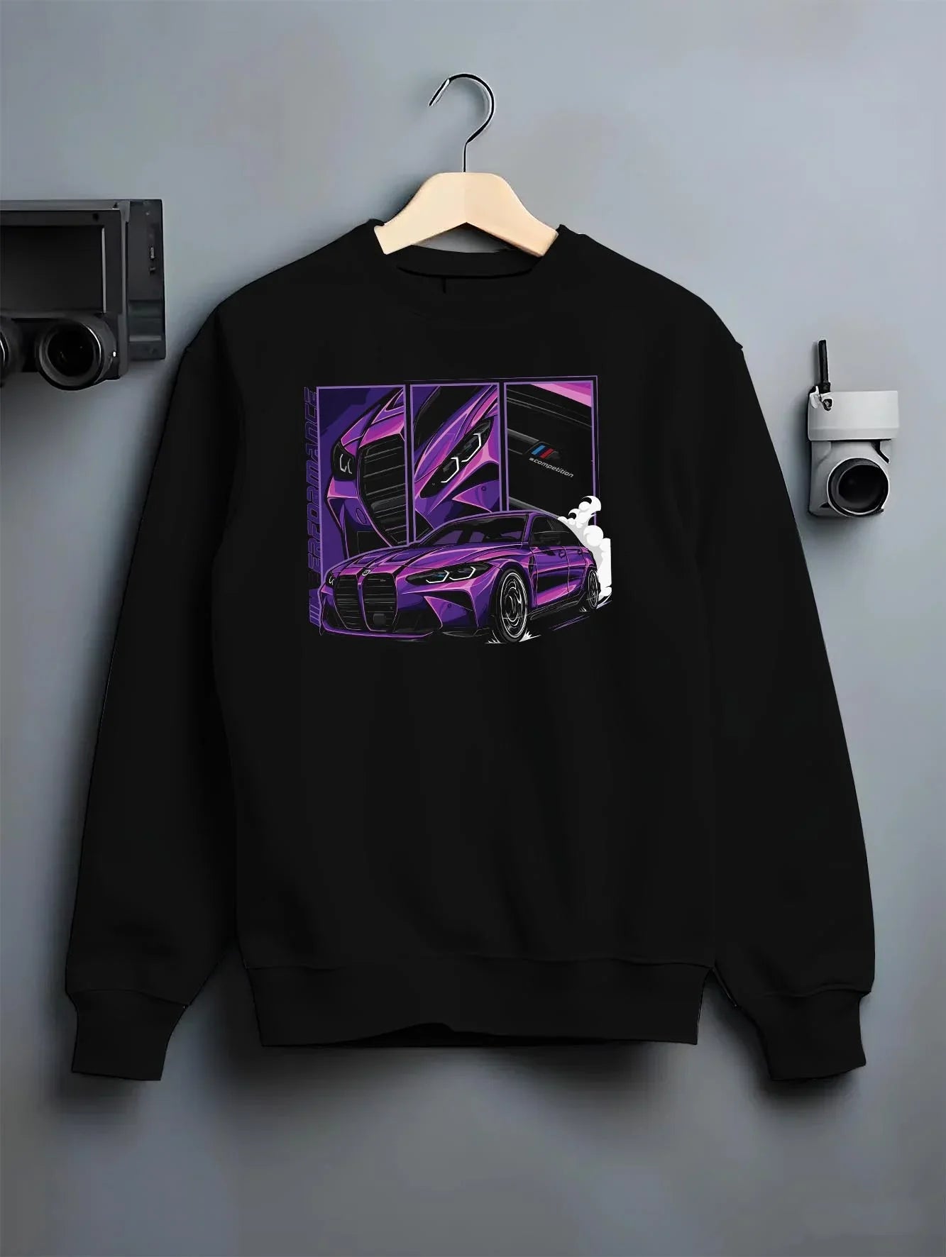 Black crewneck sweatshirt on a hanger against a grey wall, featuring BMW M4 turbo drift racing street performance graphic.