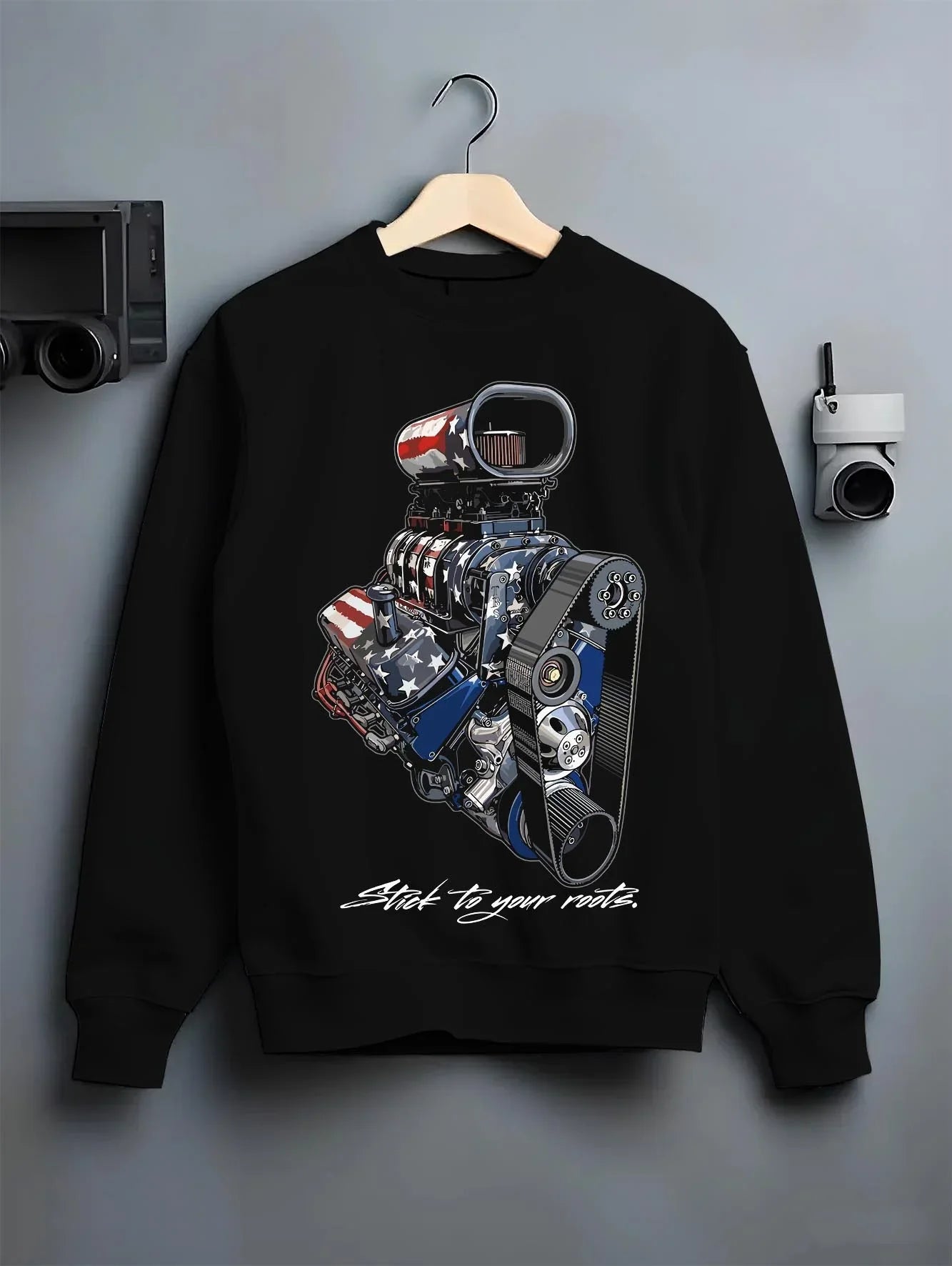 Black crewneck sweatshirt on a hanger against a grey wall, featuring v8 american muscle retro classic enthusiast racing graphic.
